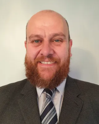 Darren Wiseman smiling, wearing a dark suit, striped shirt and tie